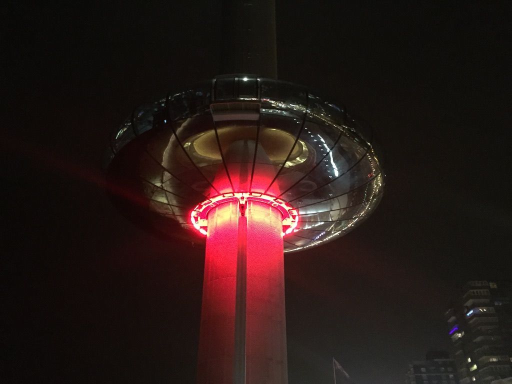 The i360 descending, underlit by red lights at night
