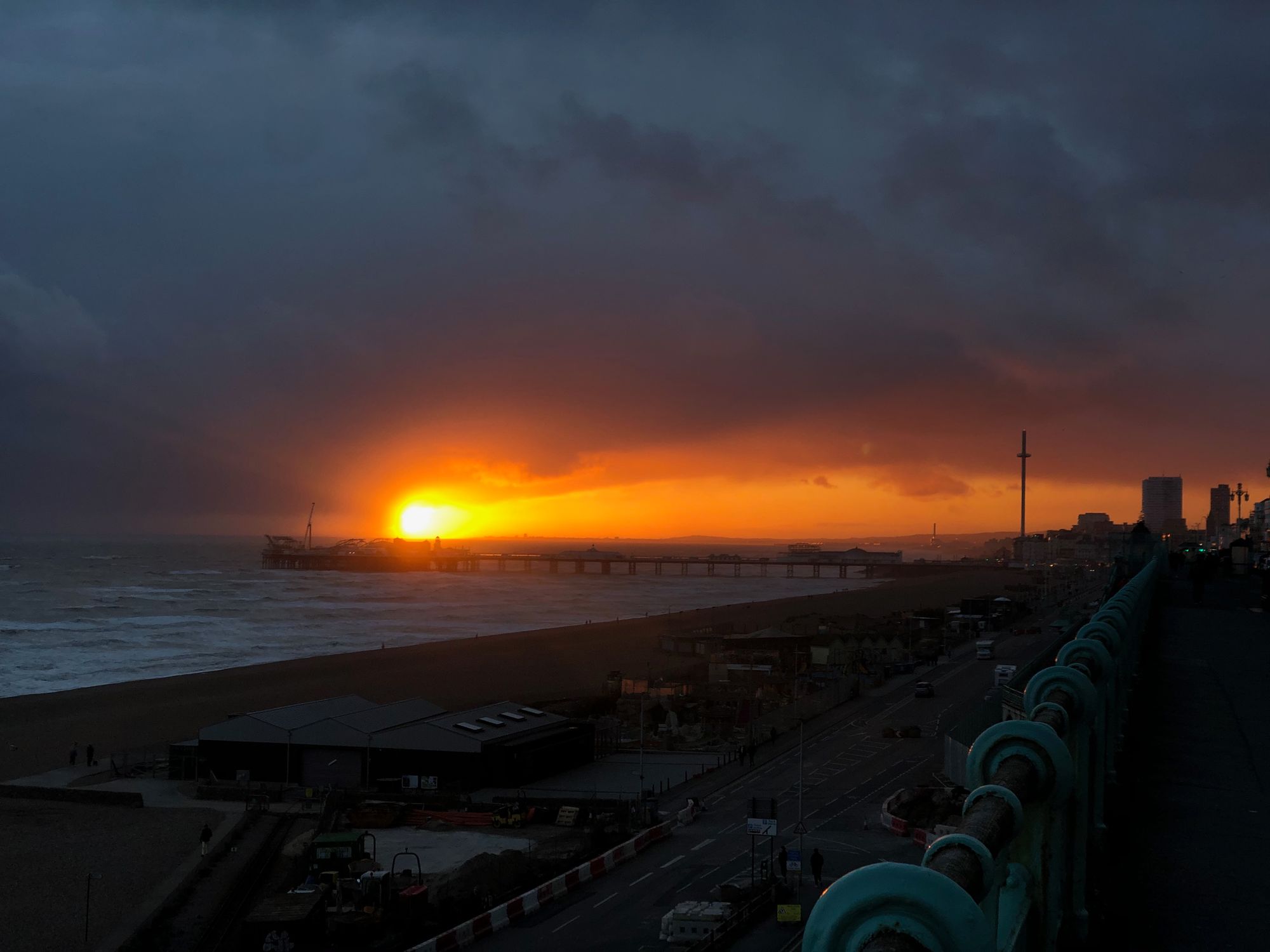 A photo of the pier as taken from Marine Parade. The sunset is bright orange, lighting a horizontal stretch of sky.