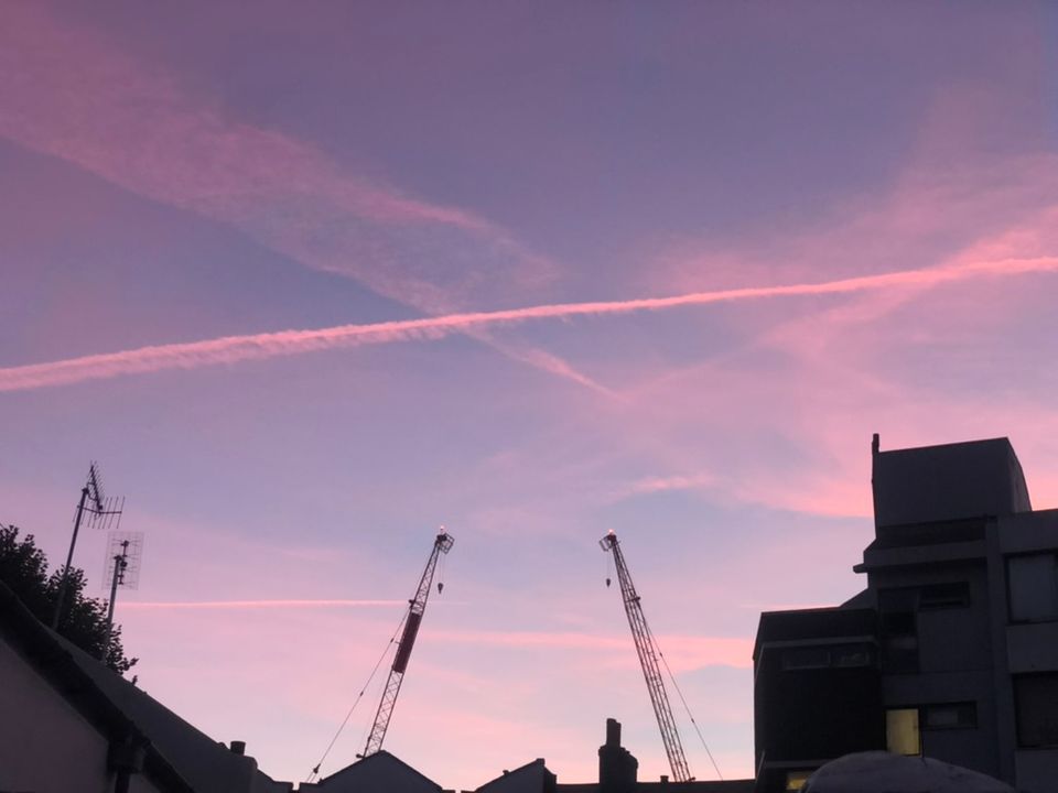 A photo of a sky filled with contrails above two cranes