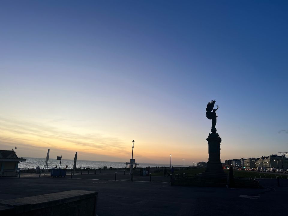 A view of the sun setting over the sea and Hove Lawns, with the Angel of Peace statue in shadow and contrasting against the b